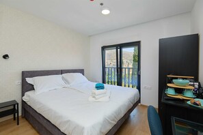 A bedroom with a bed, a window with a view, a desk with a chair, and a TV. - R5 Standard double or twin room DOMINIUM CITY SUITES (Dubrovnik)