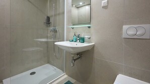 Casa de banho moderna com cabine de duche em vidro, lavatório branco com espelho em cima e sanita.