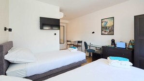 Quarto de hotel com duas camas, uma escrivaninha, uma cadeira, uma televisão e um quadro na parede.