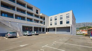 Un estacionamiento con coches, un edificio de varios pisos y balcones, y montañas al fondo.