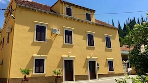 Un edificio amarillo con varias ventanas y puertas, techo de tejas y una calle en su parte frontal.