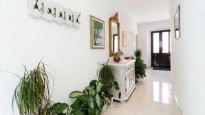 A hallway with white walls, a white console table, and several potted plants.
