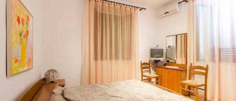 A bedroom with a bed, a desk, a chair, a television, and a mirror.