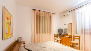 Un dormitorio con cama, escritorio, silla, televisor y espejo.