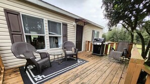 Une terrasse en bois avec deux chaises et une petite table, un barbecue et un espace abrité.