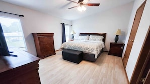 Une chambre à coucher comprenant un lit, une commode en bois, des tables de chevet et un ventilateur de plafond.