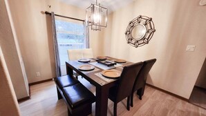 Un coin repas avec une table en bois dressée pour quatre personnes, un banc, une suspension et un miroir fixé au mur.