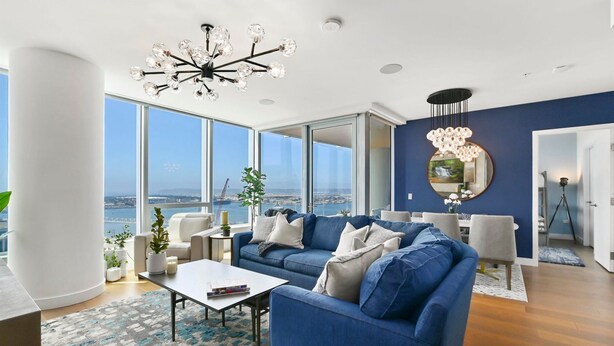 A modern living room with a blue sofa, white armchairs, and a large window offering a city view.