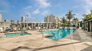 A rooftop pool area with multiple pools and lounge chairs, surrounded by palm trees and city buildings in the background.