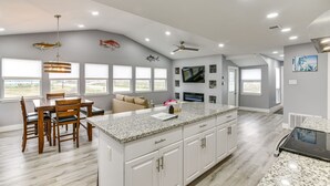 A modern kitchen with a granite countertop, white cabinetry, and a dining area with wooden chairs and a table. - Modern Freeport Home w/ Views: Walk to Beach! (Freeport)