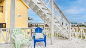 A wooden deck with two Adirondack chairs, a yellow building, and a white staircase. - Modern Freeport Home w/ Views: Walk to Beach! (Freeport)