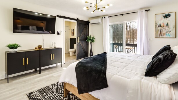 Camera da letto moderna con un letto grande, una TV a parete, un armadio con ante scorrevoli e vista all'esterno.