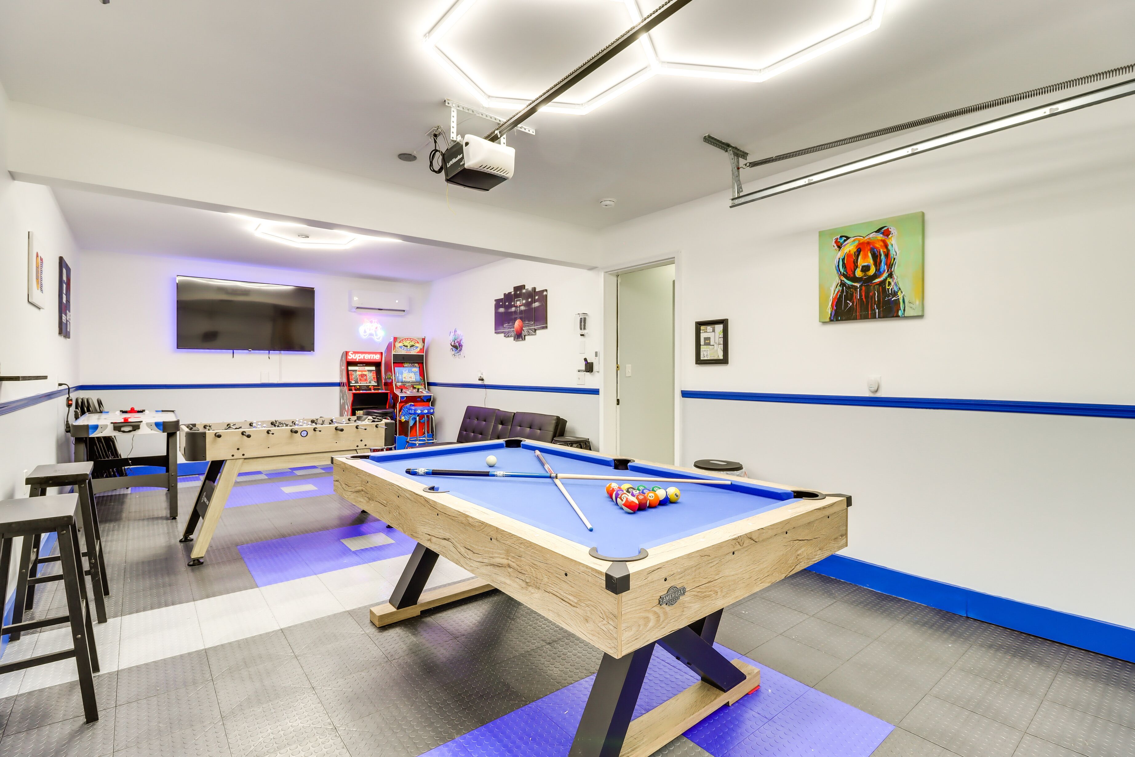 Mesa de bilhar com mesa de futebol de mesa e uma TV em um espa ço com detalhes em azul e projetor no teto.