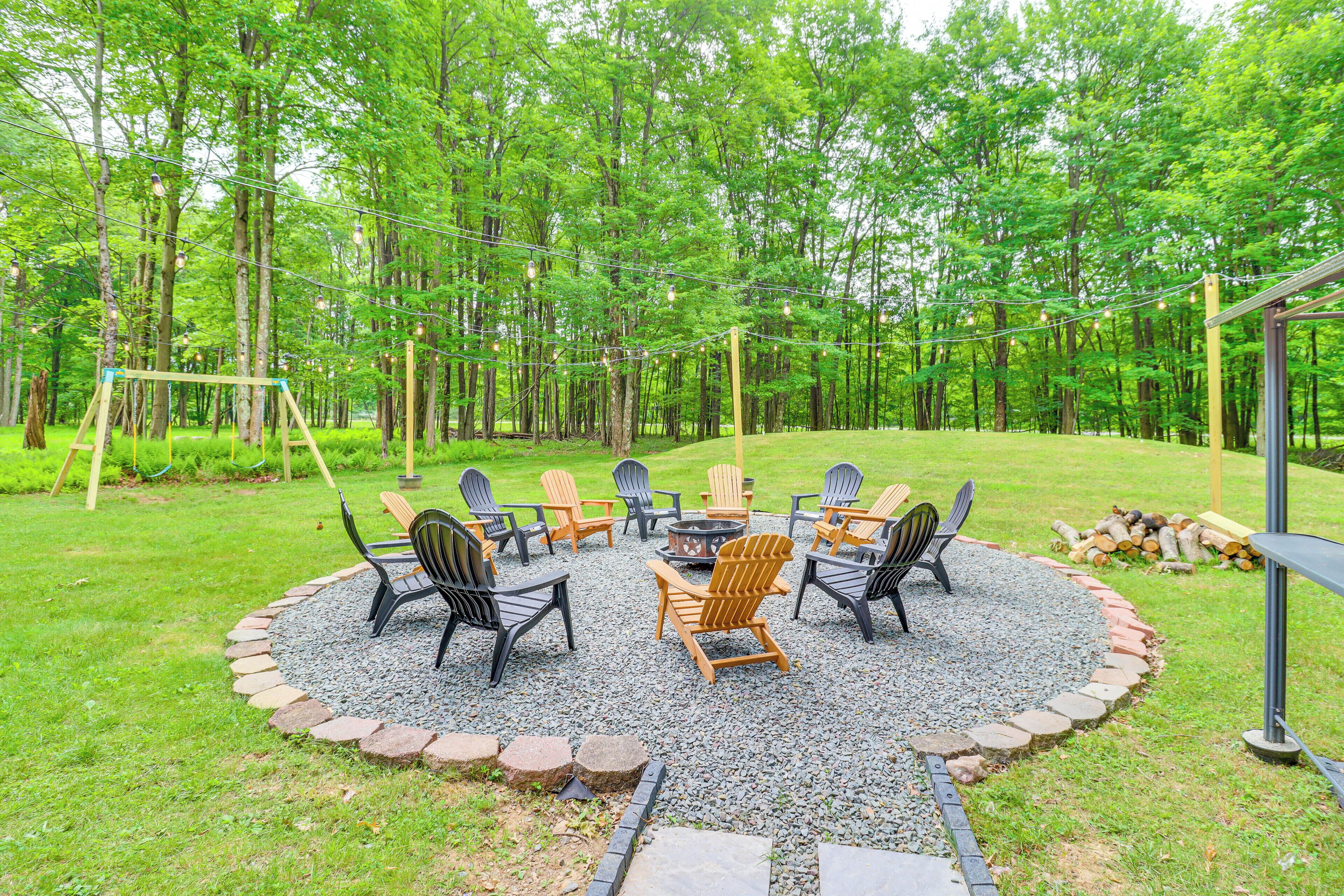 A circular outdoor seating area with Adirondack chairs and a fire pit, surrounded by a gravel circle and a stone border, set in a forested backyard.