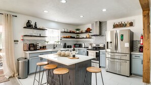 Una cucina moderna con isola centrale, sgabelli da bar, elettrodomestici in acciaio inossidabile e oggetti decorativi sugli scaffali.