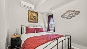 Ein Schlafzimmer mit einem Bett, einem Nachttisch, einer Klimaanlage, einem Gemälde und einer Wanddekoration.