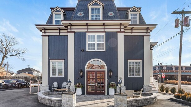 A two-story building with a dark facade, a central arched entrance, and a small porch with seating.