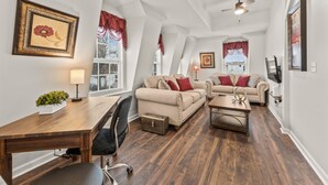 A spacious living room with high ceilings and large windows, featuring a wooden dining table, two sofas, and a coffee table.