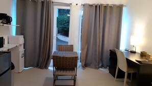 Habitación compacta con mesa y sillas, una kitchenette pequeña y un ventanal con cortinas.