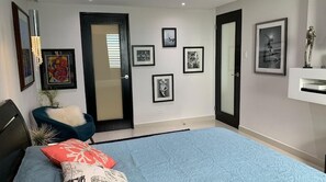 A bedroom with a bed, a chair, and a door. There are framed pictures on the wall. - Paradis - Luxurious Apartment with Ocean View and Balcony. (San Juan)