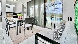 A modern outdoor dining area with a table and chairs, a grill, and a view of a swimming pool. - Oasis Retreat with Pool, BBQ & Game Room, International Drive, Near Universal (Orlando)