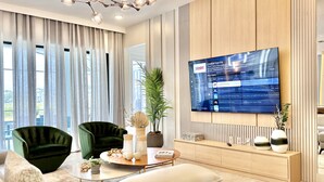 A modern living room with a large flat-screen TV mounted on the wall, a green armchair, a white sofa, and a wooden console table with decorative items. - Oasis Retreat with Pool, BBQ & Game Room, International Drive, Near Universal (Orlando)