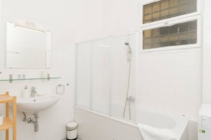 Enjoy a refreshing shower in the bathroom, featuring a clear enclosure, a sink with a glass shelf, and a bathtub.
