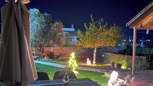 Un espace extérieur aménagé en terrasse, avec une table et des chaises, un coin salon abrité et un jardin bien éclairé agrémenté d’une fontaine.