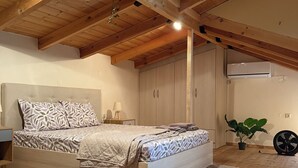 Une chambre avec un plafond en bois, un lit avec une literie à motifs, une plante en pot et un ventilateur.