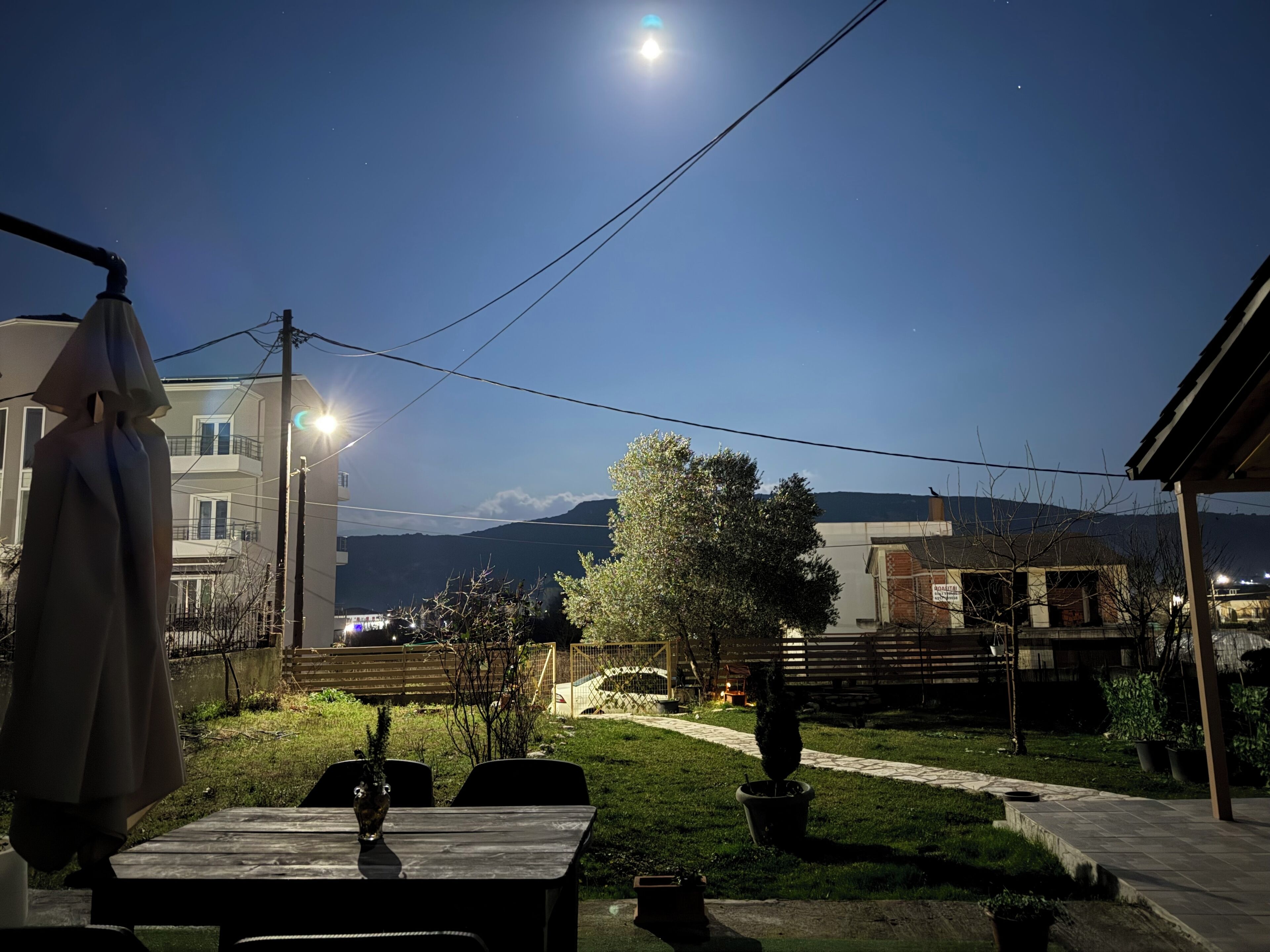 A patio area with a table and chairs, a potted plant, and a view of a building with a balcony and a mountain in the background.