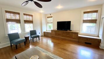 A spacious living room with hardwood floors, a ceiling fan, a flat-screen TV, and a built-in entertainment unit.