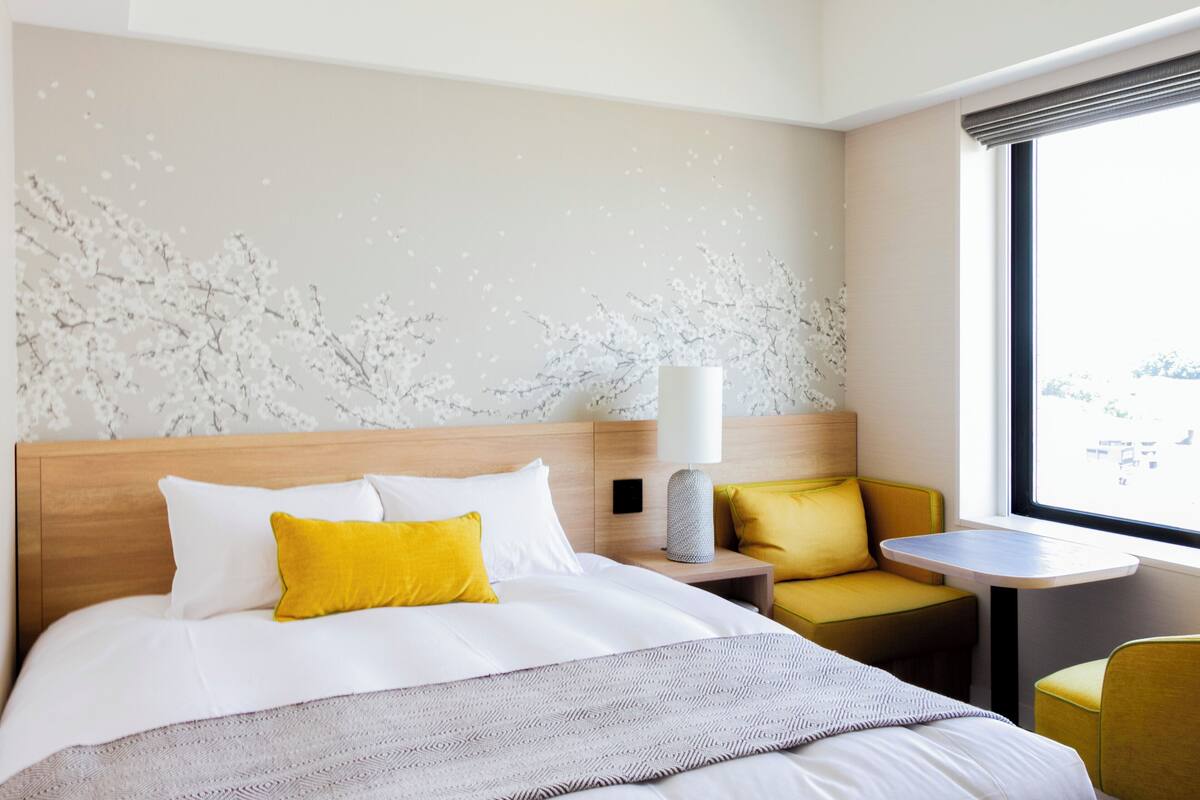 Une chambre d’hôtel avec un lit, une table de chevet, une lampe, une petite table et une chaise.