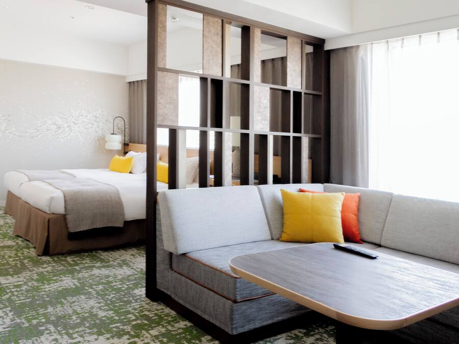 A hotel room with a bed, a sofa, a small table, and a partition.