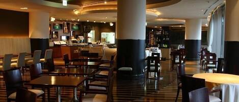 A hotel lobby with a central bar area, multiple seating arrangements, and a patterned floor.