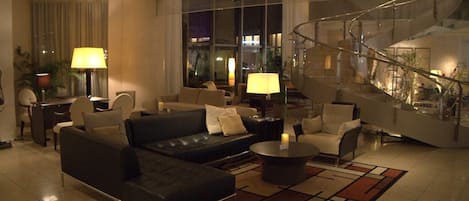 A modern hotel lobby with a black leather sofa, a coffee table, and a staircase.