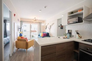 Cozy living space with a central kitchen area, featuring a coffee machine and seating area with a sofa and armchair.