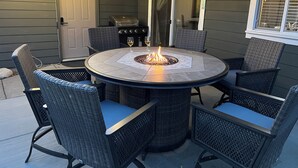 A round outdoor patio with a fire pit, wicker chairs, and a grill.