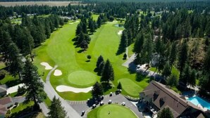 An aerial view of a golf course with a clubhouse, surrounded by dense forests and mountains in the background.