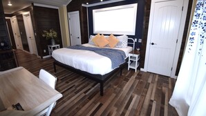 Une chambre avec un grand lit, un bureau et une chaise. Il y a deux portes et une fenêtre.