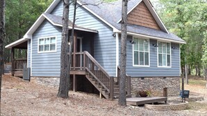 Une cabane à deux étages, avec des fondations en pierre, une terrasse en bois et un escalier menant à l’entrée.