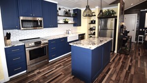 Une cuisine moderne avec des armoires bleues, des appareils en acier inoxydable, un îlot en marbre et un plancher en bois.