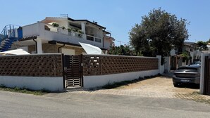 A residential area with a gated entrance, a multi-story house with balconies, and a parked car. - Double room with private bathroom (Santa Domenica di Ricadi)