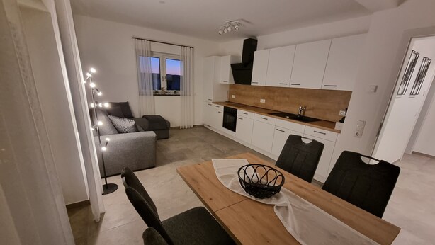 A modern living room with a sofa, a dining table with chairs, and a kitchen area with cabinets and a stove.