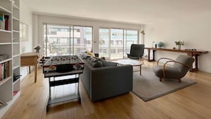 A spacious living room with a foosball table, a sofa, a chair, and a bookshelf.