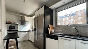 A modern kitchen with white cabinets, stainless steel appliances, and a large window providing a view of residential buildings.