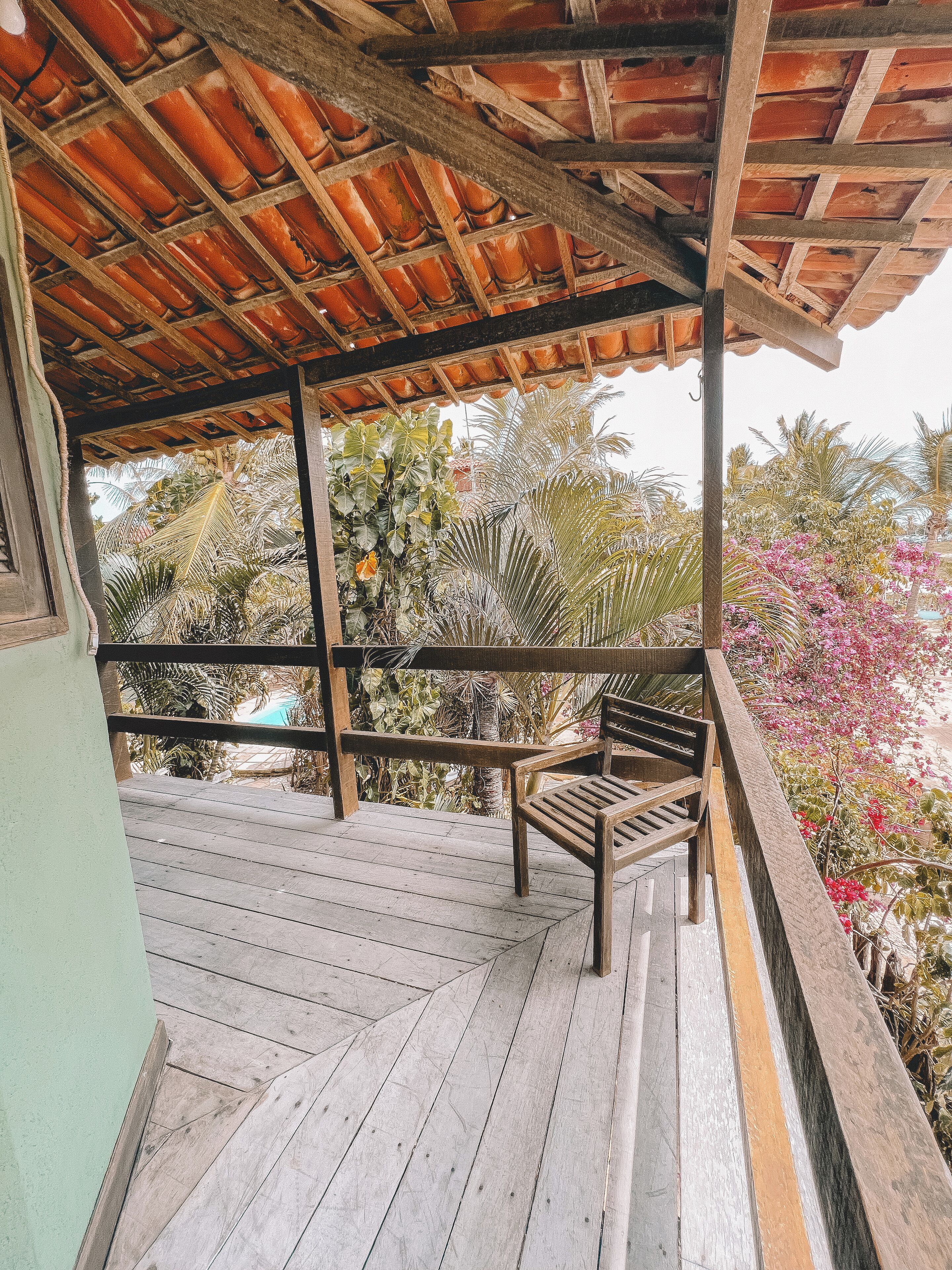Terraza de madera con un banco, rodeada de plantas tropicales y una estructura de techo de madera.