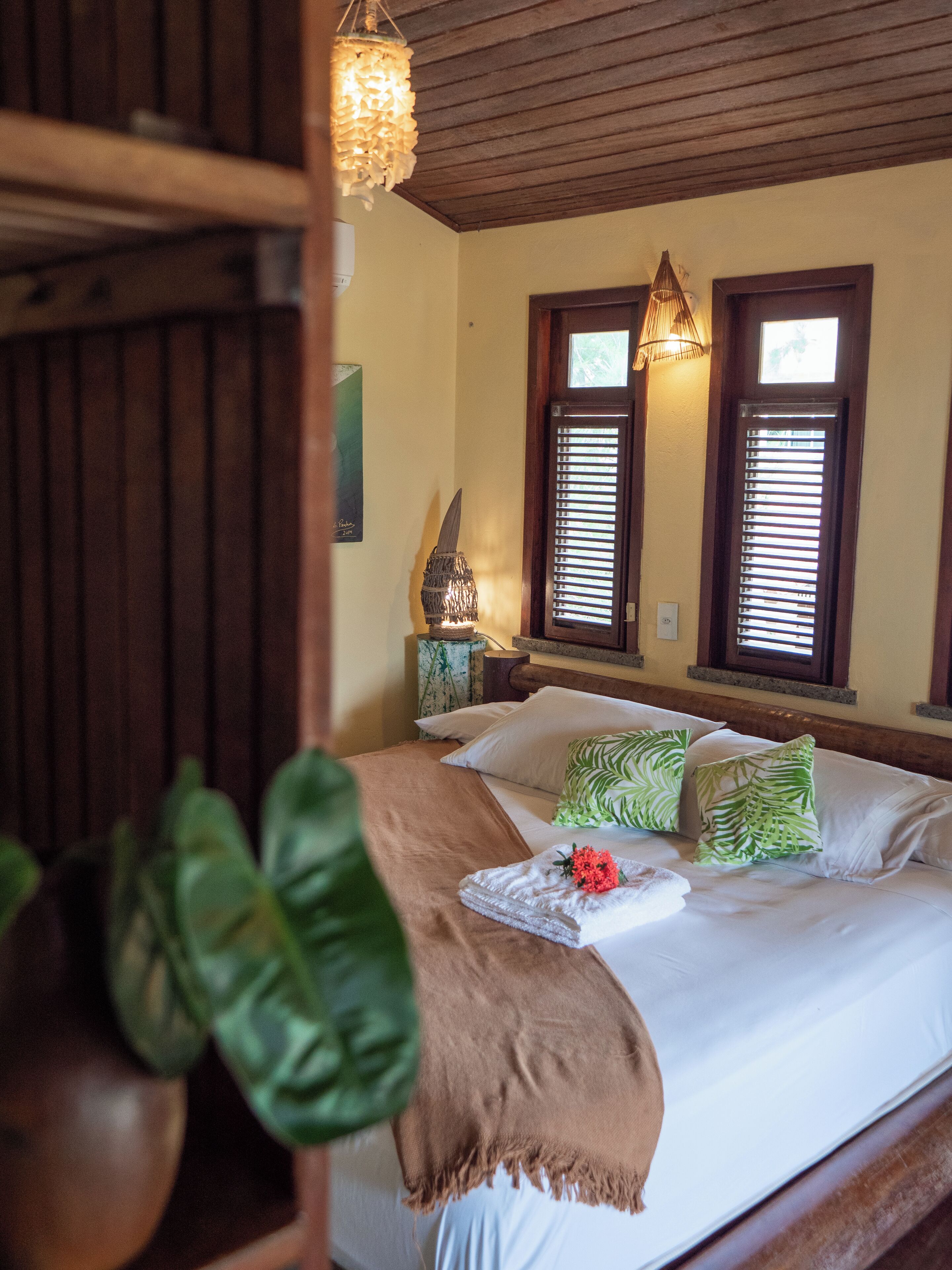 A bedroom with a bed, pillows, a nightstand, a lamp, and a window with blinds.