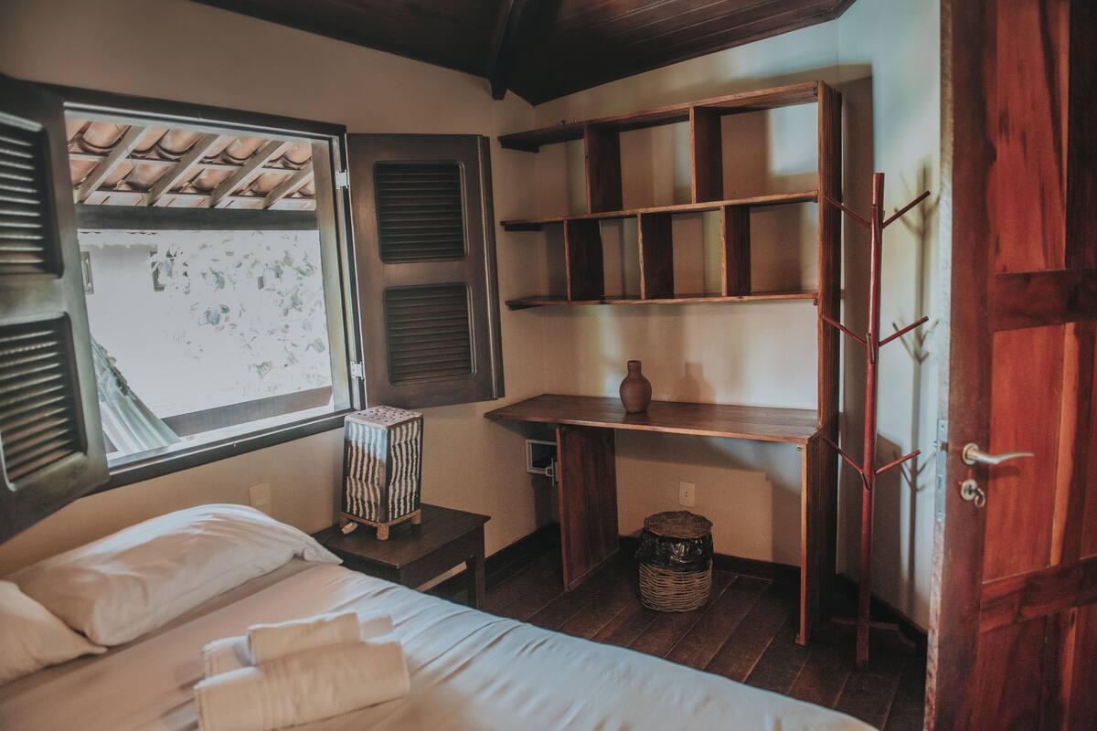 Un dormitorio con una cama, un escritorio de madera, una ventana con contraventanas y una puerta.