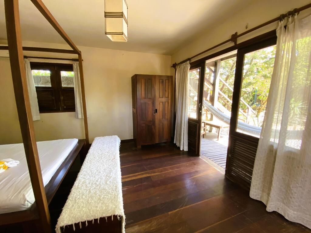 Una habitación con una cama de madera, un banco, un armario y una ventana con cortinas.
