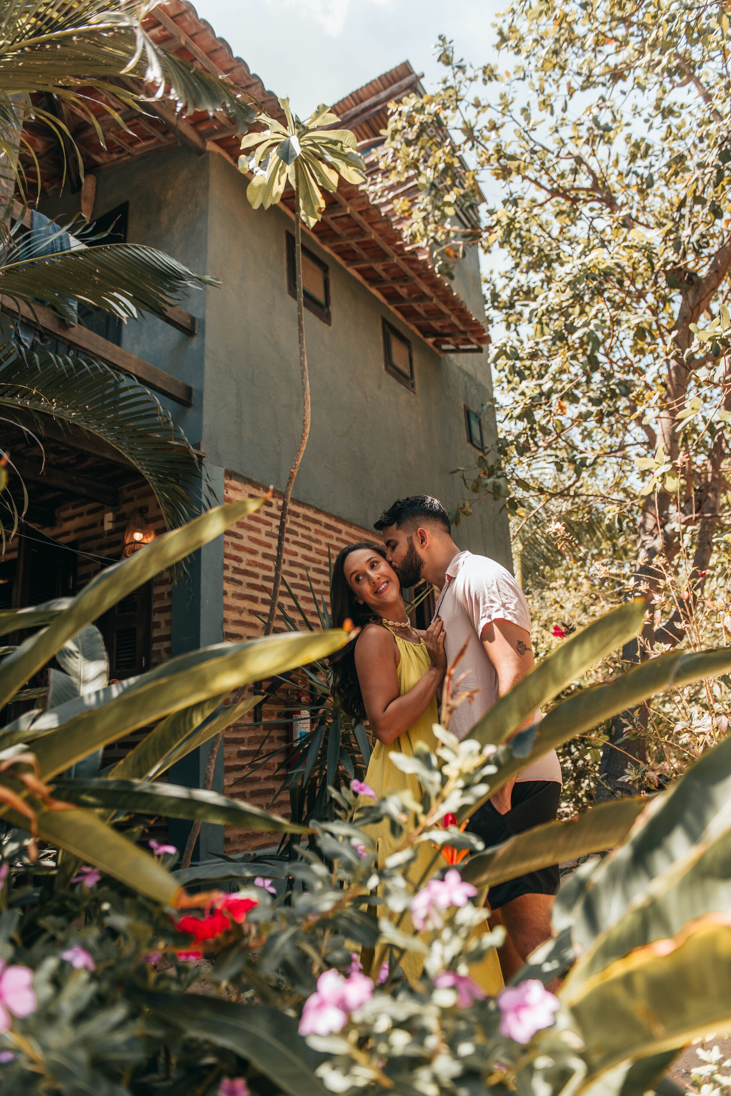 A couple embracing in a garden with a building in the background.